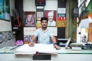 un homme assis au bureau avec un livre dans l'établissement Hotel Ashirwad DX, à New Delhi