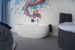 - une baignoire dans une chambre avec une fresque murale représentant une vague dans l'établissement Hotel Rauw aan de Kade, à IJmuiden