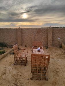 3 Stühle und ein Tisch im Sand in der Nähe einer Wand in der Unterkunft Friendo's House & Hot Spring in Siwa