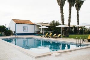 a swimming pool with chairs and umbrellas next to a house at Humus Farm in Águas de Moura