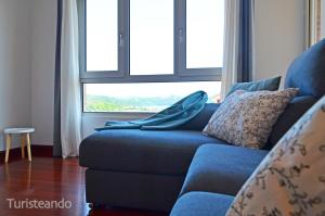 Sofá azul en la sala de estar con ventana en Apartamento La Barquera - Muy acogedor con vistas a la Ría en San Vicente de la Barquera