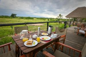 a wooden table with food and drinks on a deck at Kazinga Wilderness Safari Camp in Kasese
