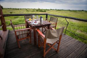 Kazinga Wilderness Safari Camp في كاسيزي: طاولة وكراسي خشبية على سطح خشبي
