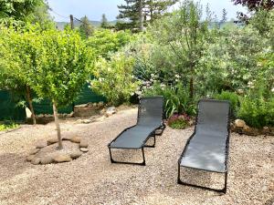 two black chairs in a garden with a tree at La rocaille du château in Gréoux-les-Bains