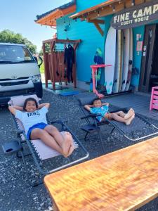 dos chicas tumbadas en sillas de jardín frente a un edificio en Finecamp Guesthouse Share Room 相部屋, en Miyazaki