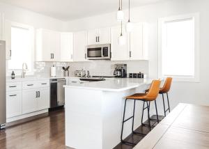 a white kitchen with white cabinets and orange bar stools at Tranquil River Home in Asheville