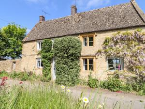 ein altes Steinhaus mit Blumen davor in der Unterkunft Woodbine Cottage in Moreton-in-Marsh