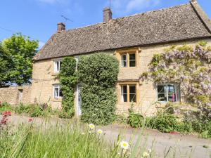 an old stone house with flowers in front of it at Woodbine Cottage in Moreton in Marsh