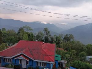 una casa con techo rojo con montañas al fondo en Kalimpong View Homestay, en Kalimpong