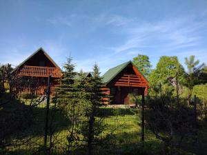 two wooden cabins in a field behind a fence at Czerwona Woda in Karłów