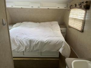 Cama blanca en habitación pequeña con ventana en Private Camper on Working Ranch, en Salida