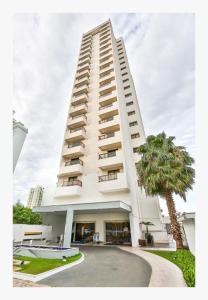 un grand bâtiment blanc avec un palmier devant lui dans l'établissement MG Flats Hotel & Residence, à Cuiabá