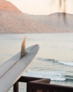 a surfboard sitting on a railing with a surfer in the ocean at The O Experience - Tayourt Lodge in Imsouane
