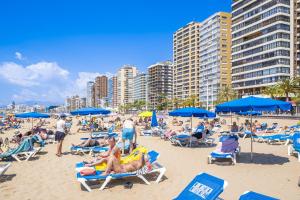 een groep mensen op een strand met blauwe parasols bij Gemelos 23 Apartment 5-A Levante Beach in Benidorm