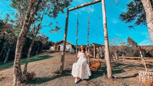 a woman in a white dress sitting on a swing at Chalé Caminho do Sol in Rancho Queimado