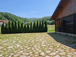 a yard with a building and a row of trees at Vikendica Una in Kostajnica
