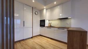a kitchen with white cabinets and a clock on the wall at Bright & Comfy - Baltea Apartments in Gdańsk