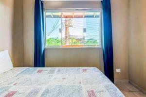 1 dormitorio con 1 cama y una ventana con cortinas azules en Chalés Ilhabela Esmeralda, en Ilhabela