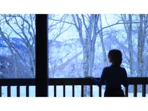 une femme debout devant une fenêtre dans l'établissement Sukayu Onsen Hakkoda Hotel - Vacation STAY 66846v, à Aomori