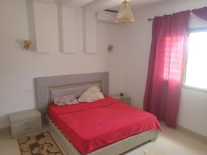 een slaapkamer met een bed met een rood dekbed en een raam bij Villa Château D'eau Djerba in Awlād ‘Umar