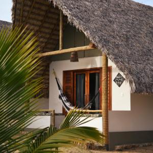 a house with a thatch roof and a hammock outside at Chalé Vera Ar condicionado Pousada 35knots Brasil in Luis Correia