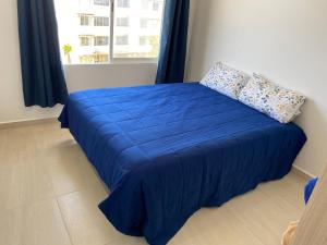 a blue bed in a room with a window at Nuevo Departamento con Excelente Ubicación y Muy Bonita Alberca - Residencial Almarena II in Mazatlán