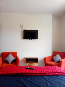 オアハカにあるCasa del Pibe Piolaのベッドルーム1室(赤い椅子2脚、壁掛けテレビ付)