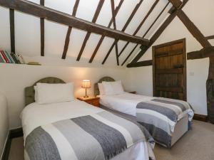 two beds in a room with wooden ceilings at Lower Court Byre in Kinsham