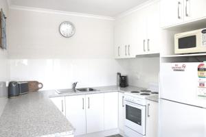 a white kitchen with white appliances and a clock on the wall at Calendo Apartments in Merimbula