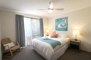 a bedroom with a bed and a chair and a window at Calendo Apartments in Merimbula