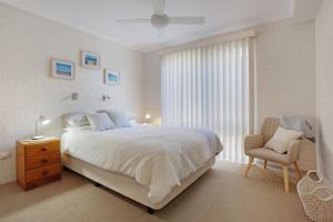 a white bedroom with a bed and a chair at Calendo Apartments in Merimbula