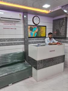 a man sitting at a counter in a room with a clock at Hotel Sai Plaza, Chembur Mumbai in Mumbai