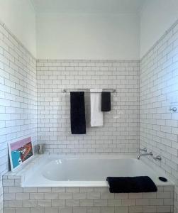 a white tiled bathroom with a tub and towels at ‘Lynton-Sur-Mer’ - Beachside Apt with Heating in Melbourne
