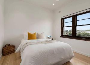 a white bedroom with a bed and a window at ‘Lynton-Sur-Mer’ - Beachside Apt with Heating in Melbourne