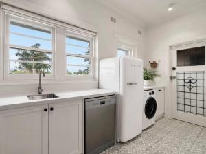 a white kitchen with a sink and a refrigerator at ‘Lynton-Sur-Mer’ - Beachside Apt with Heating in Melbourne