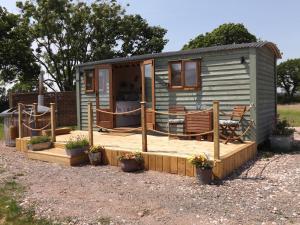 a green tiny house with a deck and chairs at Tawny in Crediton