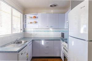 a white kitchen with a sink and a refrigerator at Cockatoo House in Sussex inlet