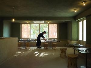 a woman standing in a room with tables and chairs at LOG in Onomichi