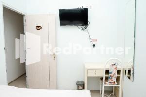 a bedroom with a desk and a tv on the wall at Happy Inn Puspo Mitra RedDoorz in Jomblang