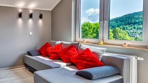 a couch with red pillows sitting in a room with windows at Apartament Szary Kamień w Świeradowie Zdrój - 5D Apartamenty in Świeradów-Zdrój