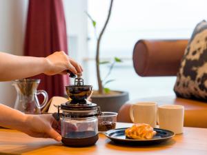 eine Person, die eine Kaffeemaschine auf einem Tisch mit einem Teller Essen verwendet in der Unterkunft Rakuten STAY Atami in Atami