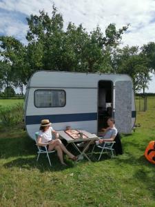 two people sitting at a table in front of a trailer at Cute little caravan for 2 in old orchard in Hem