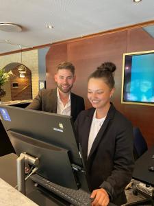 un homme et une femme debout devant un ordinateur dans l'établissement Hotel Amerika, à Hobro