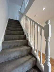 a staircase with grey carpet and white railings at The Camden Retreat in London