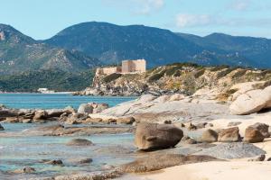 a beach with rocks and a castle in the background at Sa Guardia de Ferricci in Solanas