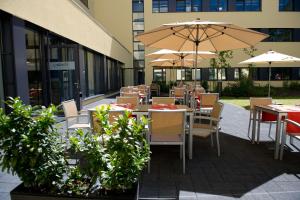 eine Terrasse mit Tischen, Stühlen und Sonnenschirmen in der Unterkunft Lindner Hotel Frankfurt Sportpark, part of JdV by Hyatt in Frankfurt am Main