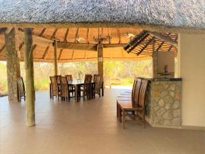 a dining area with chairs and a table and a thatch roof at Family Lodge in Natural African Bush - 2115 in Bulawayo