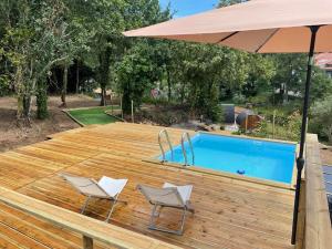 due sedie e un ombrellone su una terrazza di legno con piscina di As casinhas do Moinho a Valença