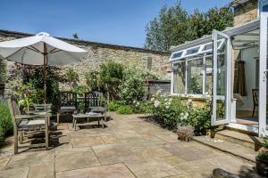 a patio with an umbrella and chairs and a greenhouse at High Trees Blenheim View in Woodstock