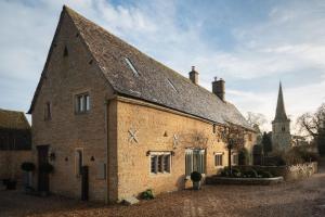 an old brick building with a church in the background at The Little Barn in Lower Slaughter